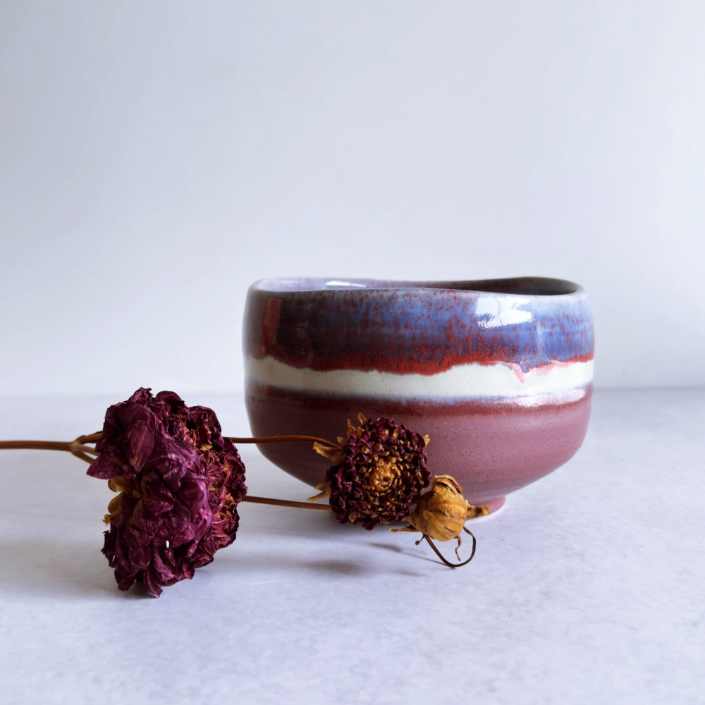 Ceramic bowl with maroon and white design on a light background with dried flowers.