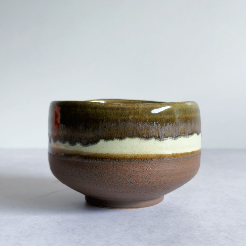 Japanese ceramic matcha bowl with multicoloured brown glaze on a white background. 