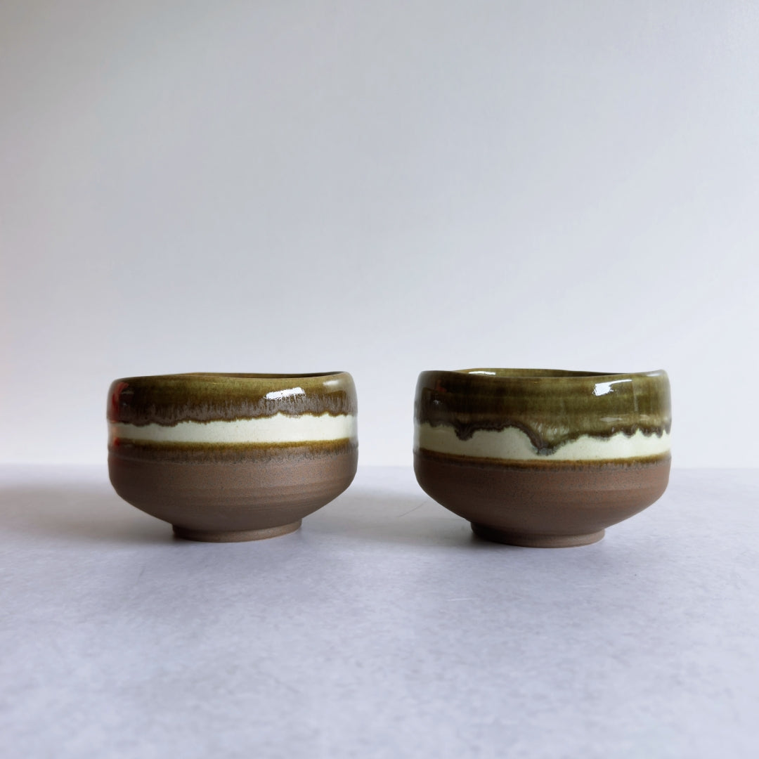 Two Japanese ceramic matcha bowls with a brown and white glaze on a light gray background