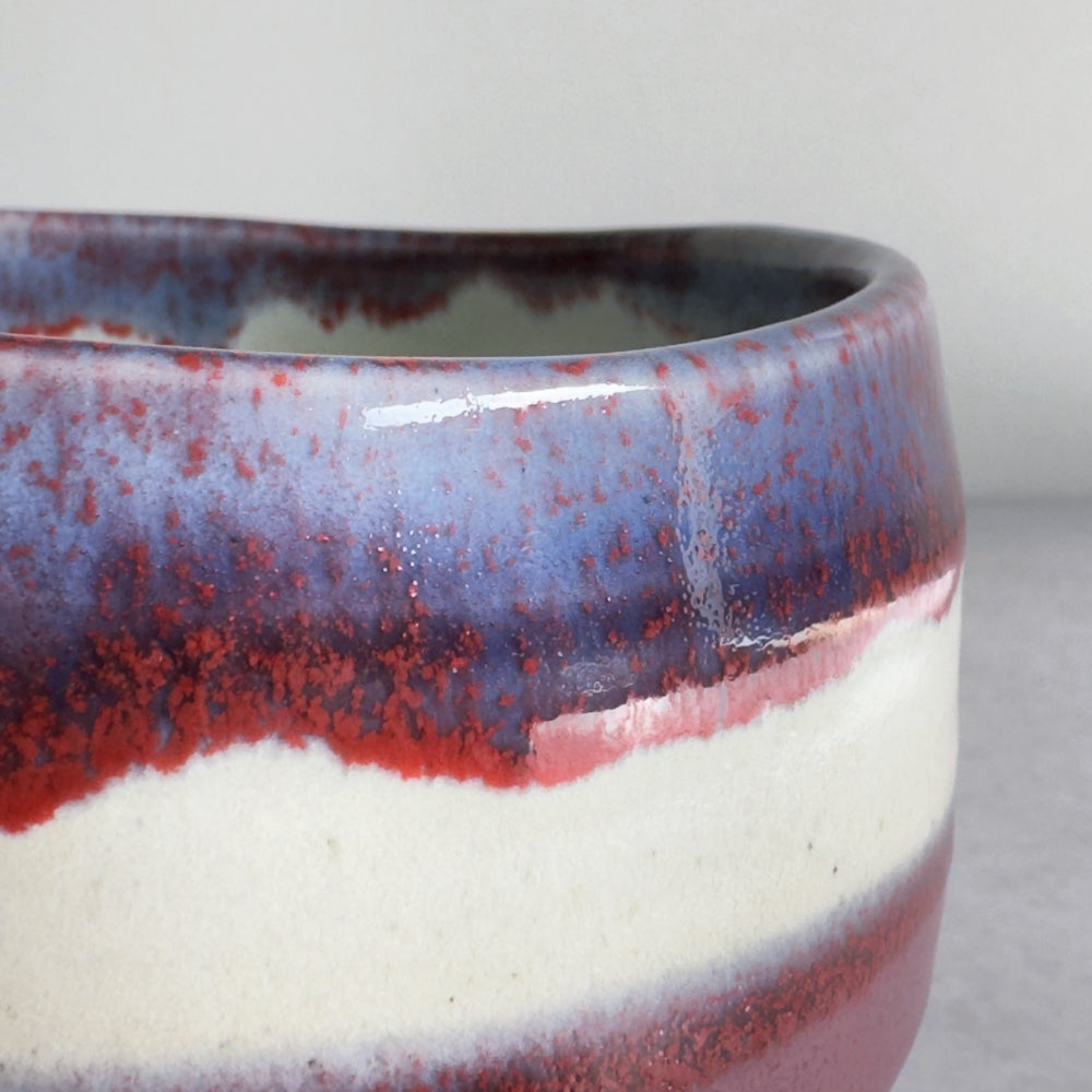 Close up of Japanese ceramic matcha bowl with purple and red glaze on a plain background
